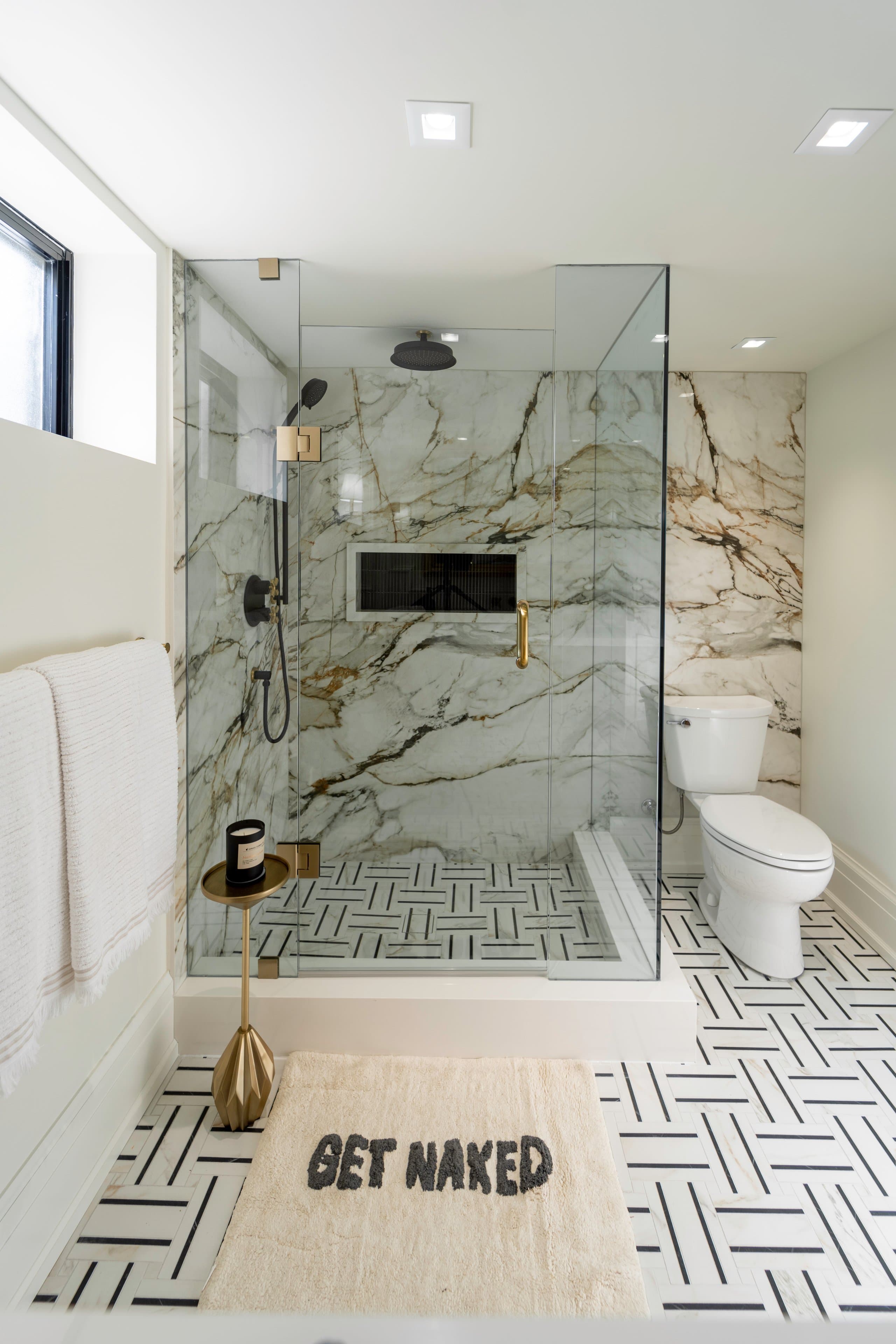 large marble slabs with striking veining on the walls, a glass enclosure, and modern brass fixtures
